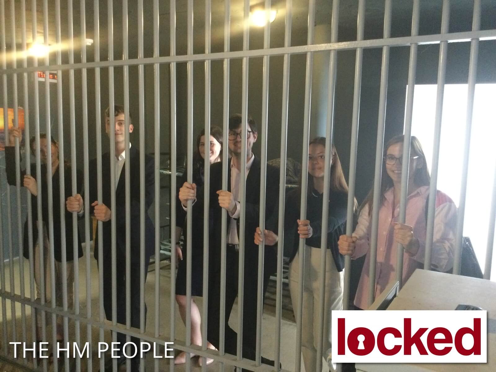 Smiling team members in an escape room, behind the bars of a cage