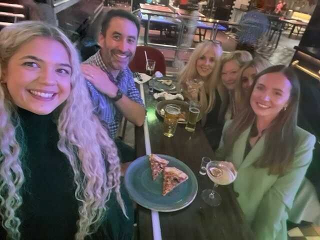 Team members sitting around a table with drinks and pizza